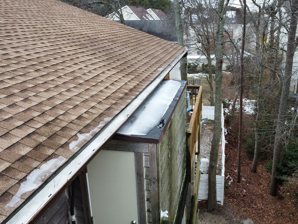 Drone view along a roof edge showing shingles, a low-slope roof section and its flashing