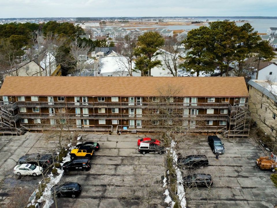 Drone photo of a three-story condominium and its parking lot, with the bay visible behind the neighborhood